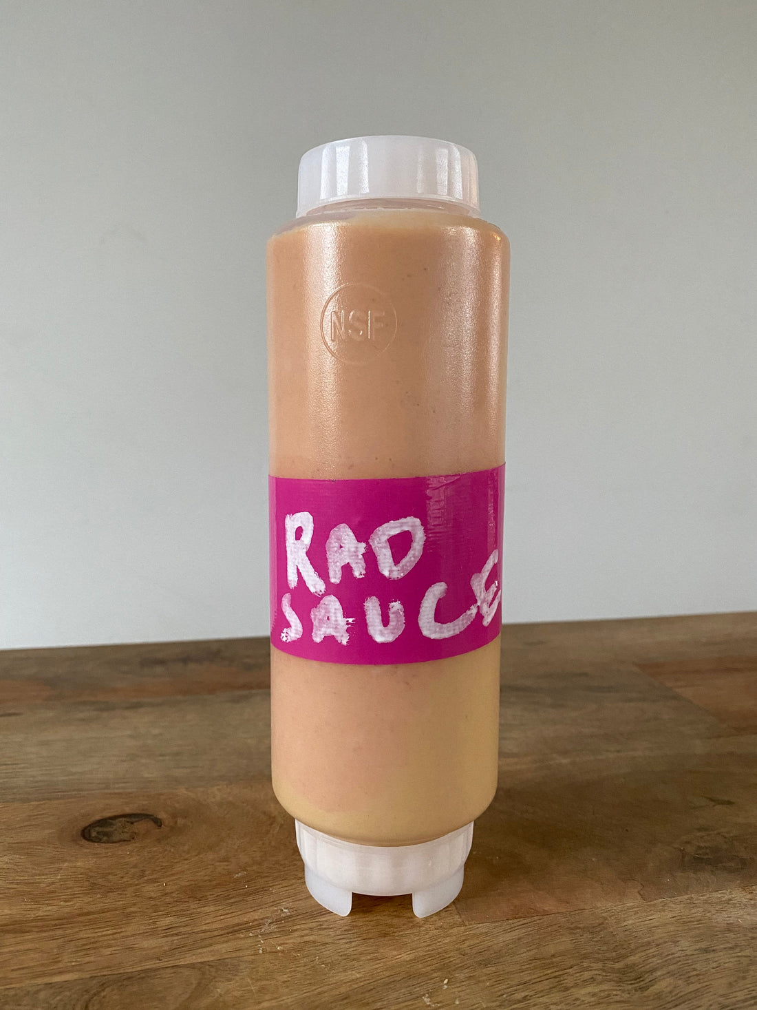 RAD sauce squeeze bottle with a pink label standing on a wooden table